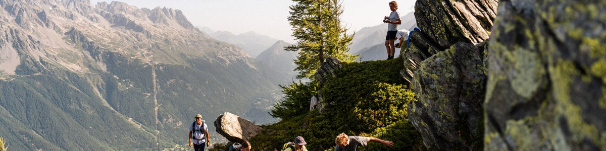 Wanderer mit Rucksäcken im Gebirge, im Vordergrund ein bemooster Felsen.