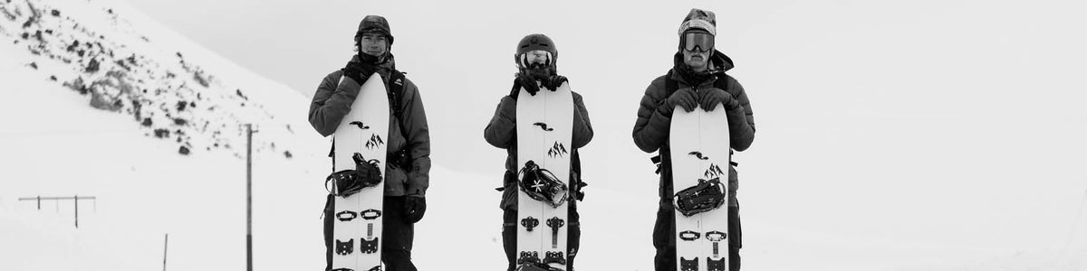Drei Snowboarder stehen mit ihren Boards im Schnee, Schwarz-Weiß-Aufnahme.