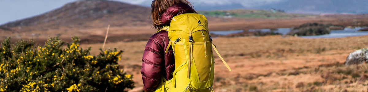 Frau trägt rote Jacke und einen gelben Wanderrucksack.