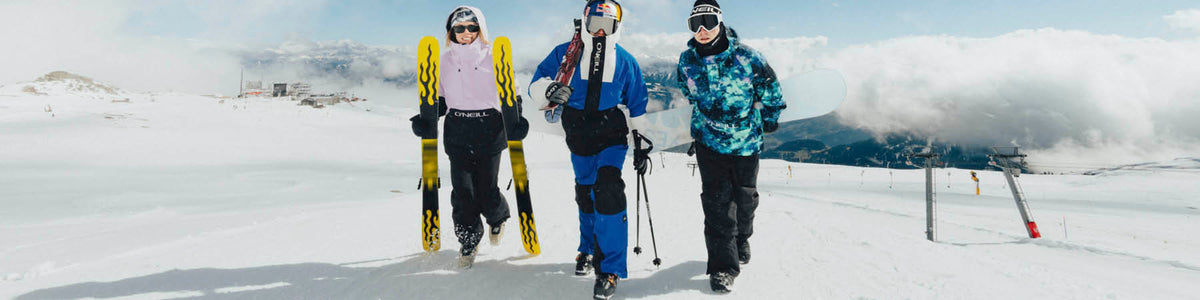 Drei Wintersportler gehen mit Ski und Snowboard über eine Piste.