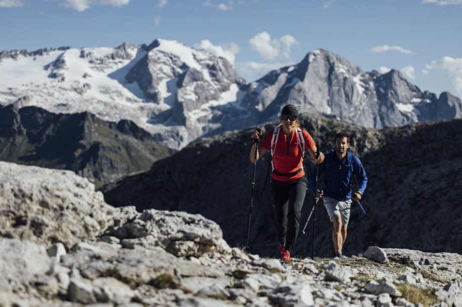 Zwei Menschen bei einer Outdoor Tour durch die Berge. Passend zur Umgebung sind sie ausgestattet mit Wanderschuhen, Wanderhosen, Wanderjacken und Wanderstöcken.