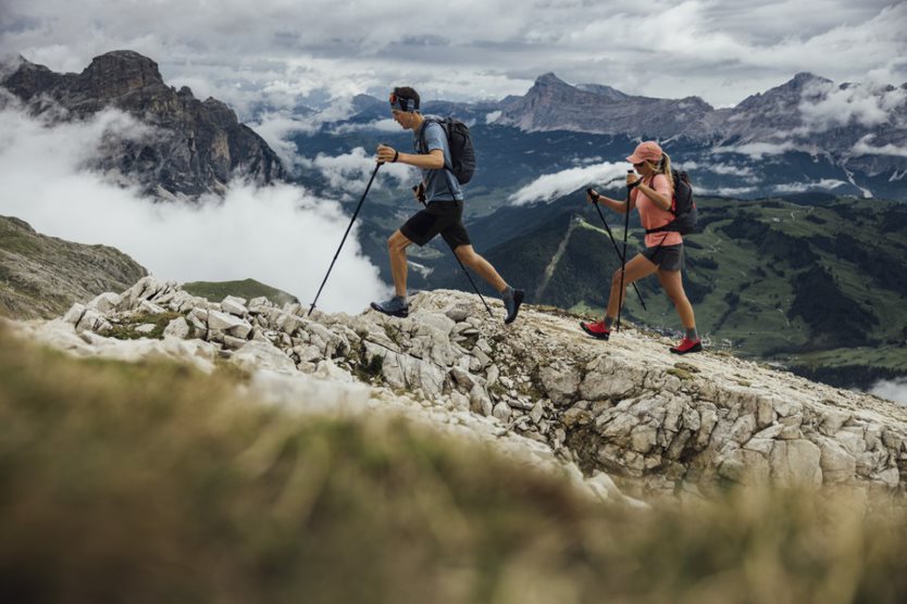 Zwei Menschen wandern mit Walking Stöcken im hohen Gebirge. Sie sind von Kopf bis Fuß ausgestattet mit der Outdoor Marke Salewa