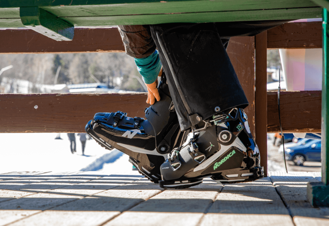Skischuhe an den Füßen eines Skifahrers, der auf einer Holzbank sitzt