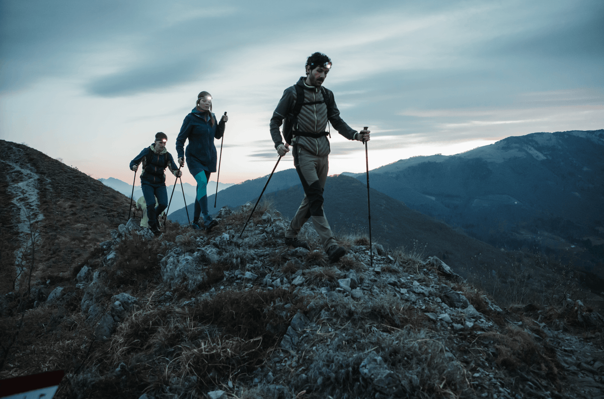 Freunde wandern einen Berg mit Wanderstöcken entlang. 