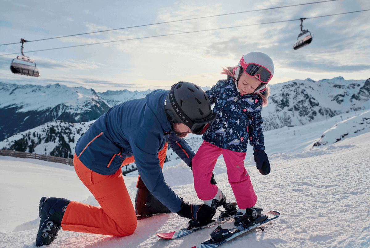 Vater hilft seiner kleinen Tochter beim Einsteigen in die Ski
