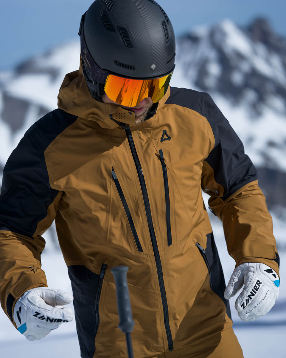 Skifahrer in brauner Hardshell-Skijacke mit Helm und orange verspiegelter Skibrille