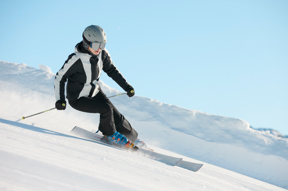 Skifahrerin in schwarz-weißem Anzug fährt eine sonnige Piste hinunter