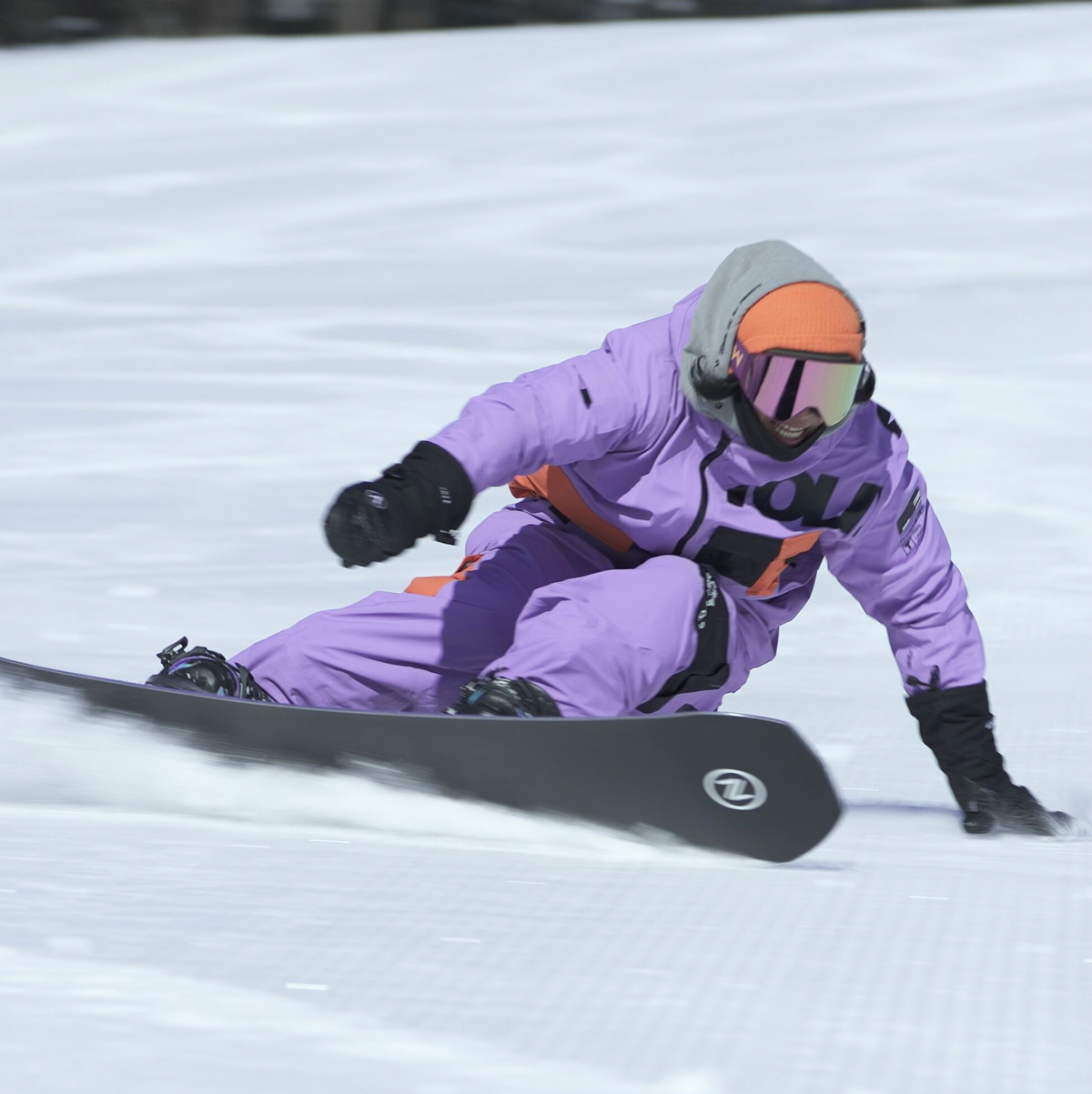 Snowboarderin in lila Anzug legt sich mit dem Board tief in eine Kurve auf der Piste
