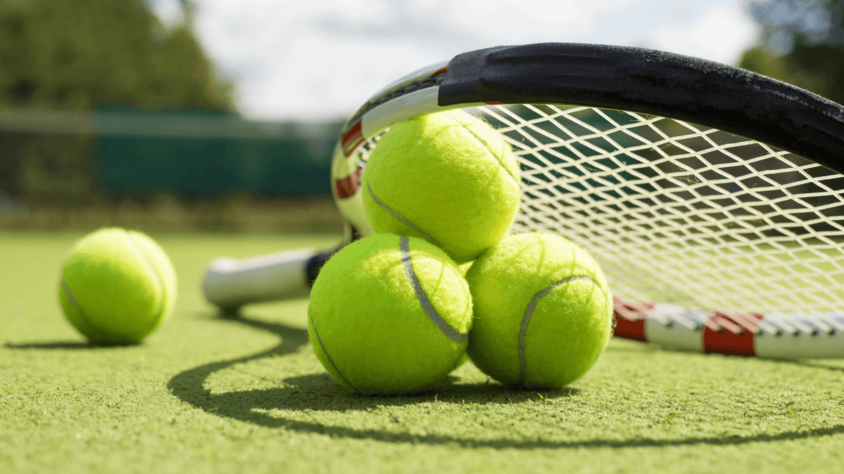 Tennisbälle und ein Tennisschläger auf dem Rasen
