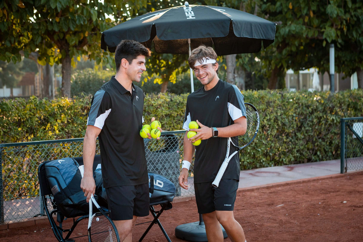 Zwei Männer halten Tennisbälle in der Hand und stehen auf dem Tennisplatz.