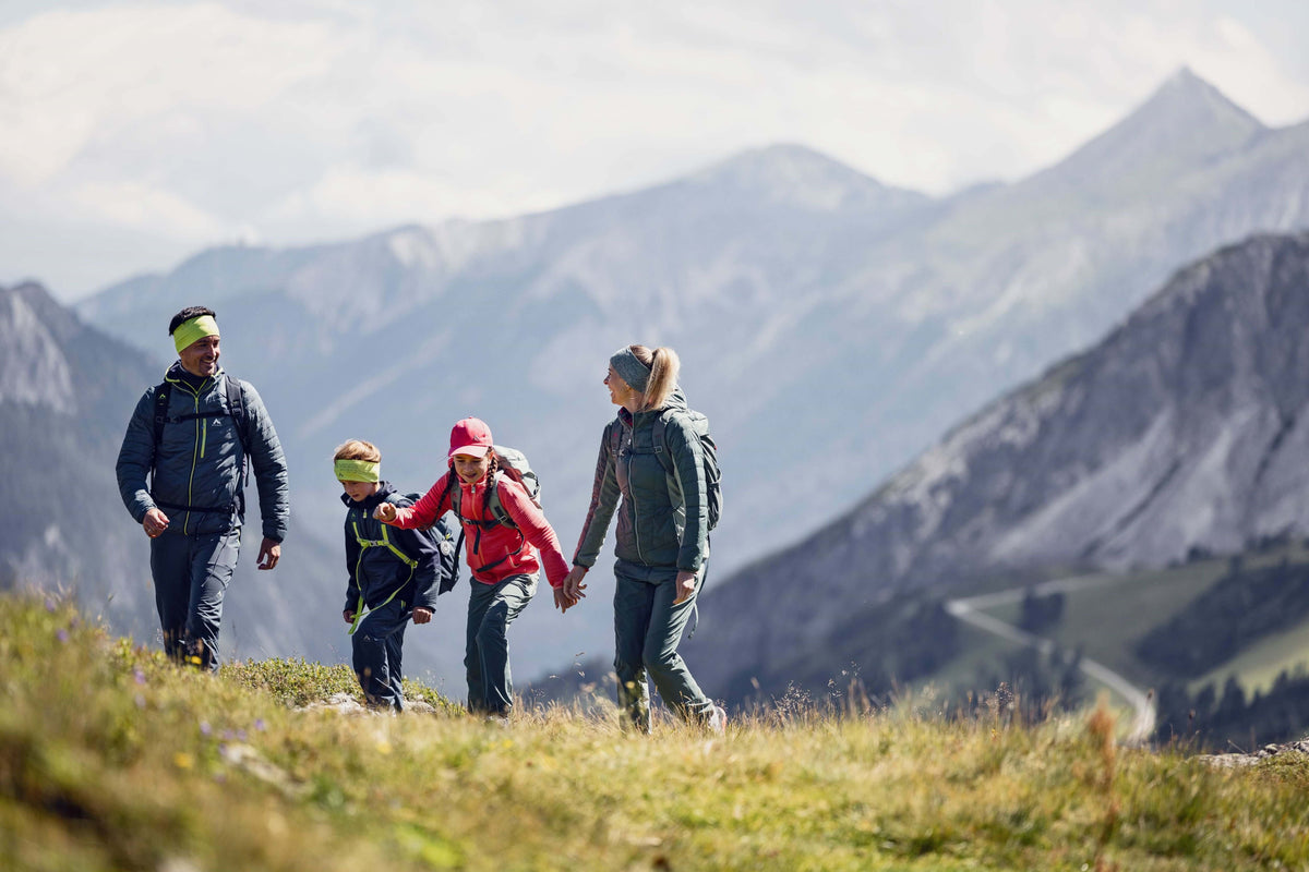 Familie mit zwei Kindern wandert Hand in Hand über eine Bergwiese